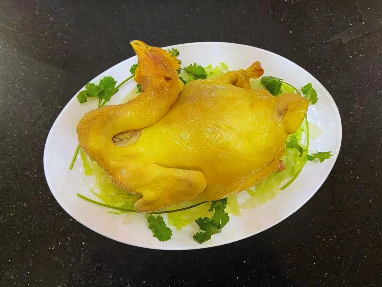 Whole poached yellow chicken garnished with lettuce and cilantro
