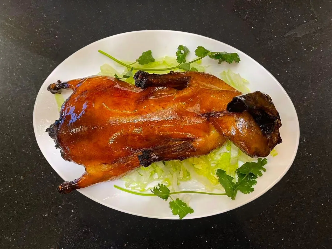 Whole roasted duck on white plate garnished with lettuce and cilantro