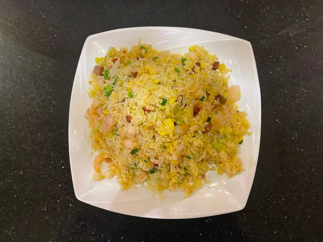 Shrimp fried rice with egg, green onion and diced meat on white plate